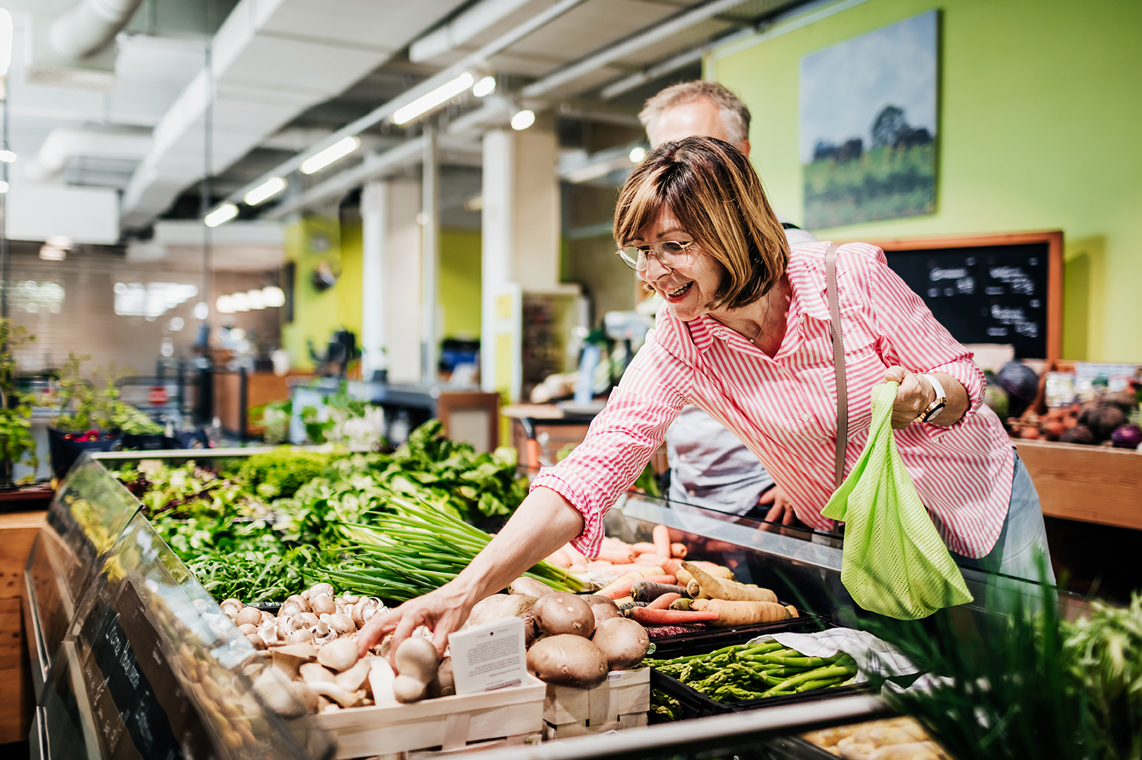 Mature Woman Reaching For Some Mushrooms While Grocery Shopping